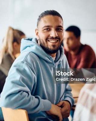 Happy college student having a lecture in the classroom and looking at camera.